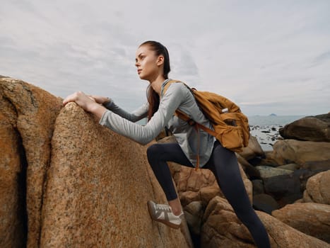 A young female hiker in sporty attire climbs rocky terrain with determination, set against a coastal landscape, ideal for adventure travel, fitness, and outdoor exploration themes