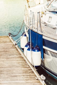 Boat docked by wooden pier with blue fenders and calm water, background