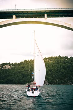 Sailboat under arch bridge on calm water, suitable for background