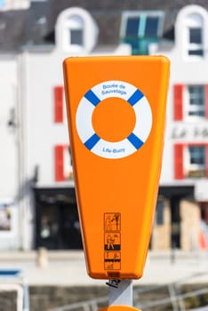Bright orange life buoy station with safety symbols in a harborside setting