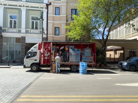 Tbilisi, Georgia, April 11, 2025: Delivery workers unload bottled beverages from Coca Cola truck on urban street, with crates of water and soda stacked inside vehicle