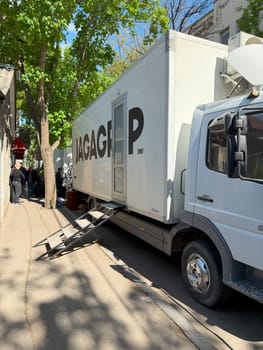 Tbilisi, Georgia, April 11, 2025: Film production truck parked on city street with stairs and equipment, used as mobile base during shooting, surrounded by crew and shade from nearby trees