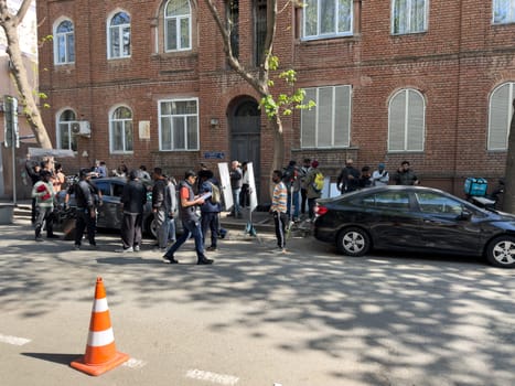 Tbilisi, Georgia, April 11, 2025: Film crew of India ethnicity shoots scene on city street near brick building, with cars, equipment and people preparing for production during sunny day