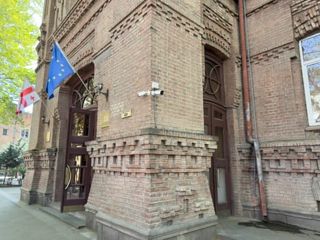 Tbilisi, Georgia, April 11, 2025: Entrance to Ministry of Education and Science of Georgia in Tbilisi with Georgian and EU flags, national emblem and historic brick architecture under daylight
