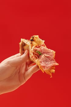 Delicious slice of pizza with prosciutto and tomato sauce held by a hand, perfect for food and lifestyle themes