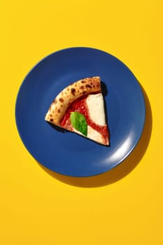 Overhead view of a single slice of pizza margherita on a blue plate against a vibrant yellow backdrop