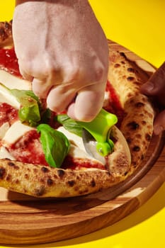 Cook slicing pizza with mozzarella, tomato and basil on wooden board