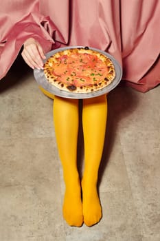 Woman wearing yellow tights presenting a salmon pizza on a tray, hidden behind a pink curtain