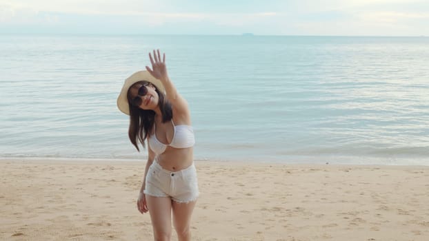 Beautiful Asian woman wear sungrass and hat turning back running to tropical paradise beach, Happy female in bikini having fun with hand to camera inviting you come with me