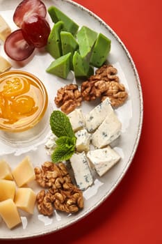 Delicious cheese plate with various types of cheese, walnuts, grapes, honey, and mint, creating a flavorful and visually appealing culinary experience