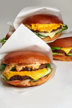 Three mouth-watering cheeseburgers with melted cheese, fresh vegetables, and sauce, served in paper wrappers
