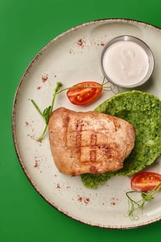 Delicious grilled chicken breast served with spinach puree, cherry tomatoes, white sauce, and microgreens on a plate