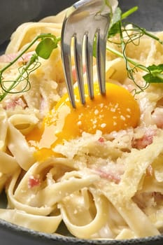 Creamy carbonara pasta with crispy bacon, grated parmesan, and a vibrant egg yolk being pierced by a fork