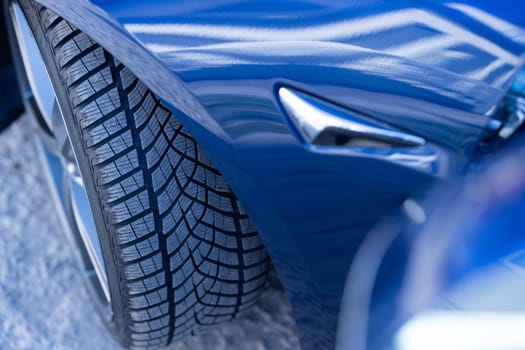 Close up winter tires on a road. Driving car with winter tire wheel on road. Detail of car tires in winter on the road. Headlight turning off switching of car LED headlights. New modern electric car.