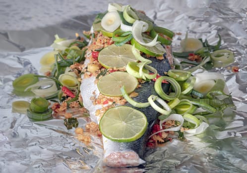 Prepare Whole Baked Salmon with Herbs on aluminium foil. ingredient include Coriander root, Ginger, Galangal, Kaffir lime, Leek, chopped together and Bird's eye chili with Slice lemons place on the Salmon fish. Healthy eating, use it as your Wallpaper, Poster and Space for text, Selective focus.