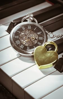 London, UK - Apr 19, 2025 - A retro pocket watch or Antique pocket watch with Golden heart shaped love padlock on Piano keys background in Vintage tone. The concept of the time of love, use it as your Wallpaper, Poster and Copy space, Selective focus.