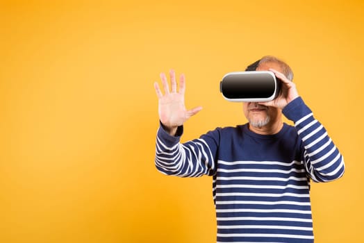Portrait Asian smiling old man touching at something in a virtual reality glasses headset studio shot isolated yellow background, Excited happy senior man pensioner using VR play simulation game