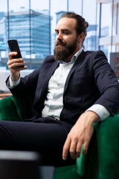 Influential businessman CEO navigating on his smartphone at the office, setting his objectives for productivity and efficiency. Young entrepreneur leads a corporation, multitasking.
