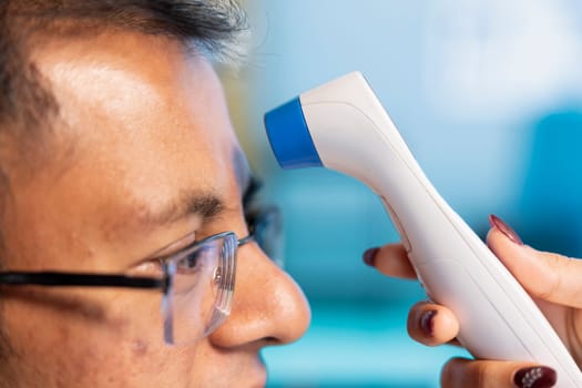 Female specialist consulting a male patient and using thermometer, measuring temperature to offer diagnostics. Indian medic doing fever measurement with a tool, check up visit. Close up.