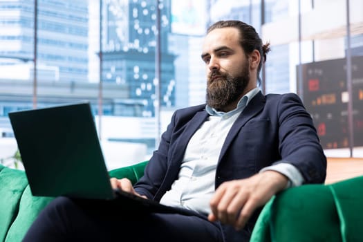 Ambitious male CEO working in a modern luxurious skyscraper, reviewing financial forecasts and tracking employees performance. Young entrepreneur navigates laptop in his office.