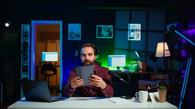 Tech expert presenting tablet in entry level low budget price range to interested viewers, filming in studio. Viral content creator reviewing digital device in front of internet audience, camera B