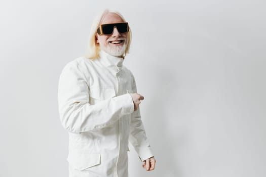 Modern man with long white hair and sunglasses, dressed in a stylish white jacket, pointing and smiling against a minimalistic white background, representing confidence and contemporary fashion