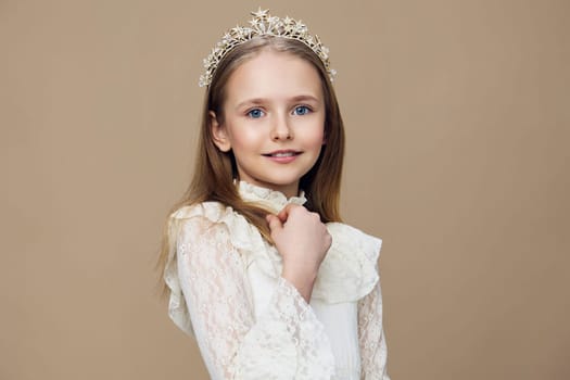 This portrait features a lovely young girl in a delicate lace dress and a crown, exuding a sense of joy and innocence The warm beige background enhances the overall softness and charm, ideal for children s portrait photography
