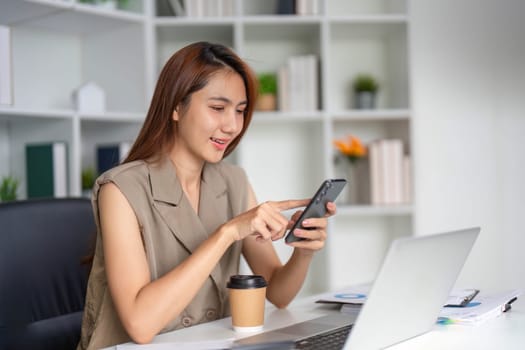 In her stylish office, a woman uses her smartphone to connect with colleagues while savoring her coffee, blending communication and technology in a dynamic environment.