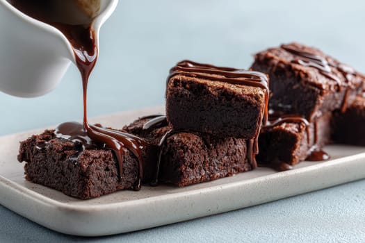 Chocolate brownies on a ceramic dish with drizzling melted chocolate sauce..