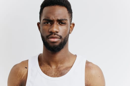 Confident african american man in white tank top gazes intensely at the camera, exuding determination and strength.
