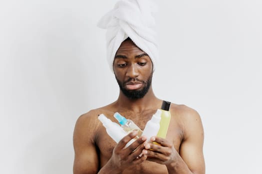Man with towel on head holding shampoo and conditioner bottles, preparing for a refreshing shower and hair care routine.