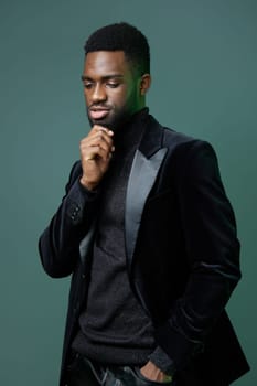 A confident young man in a black suit, hand on chin, gazing intently at the camera, deep in contemplation.