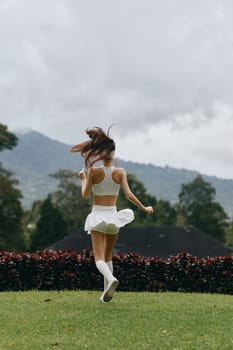 A happy young woman in a white outfit dancing in a meadow, with mountains in the background, capturing the essence of joy, freedom, and outdoor lifestyle during spring