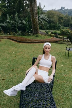 A young woman exudes tranquility while wearing modern white activewear, resting in a lush garden, symbolizing wellness, relaxation, and a healthy lifestyle