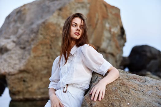 Serene woman in flowing white dress strikes confident pose on ocean rock