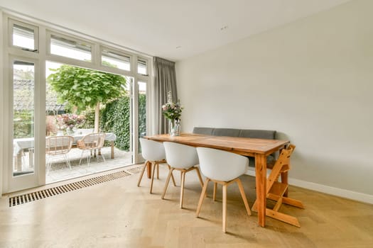 Bright and contemporary dining area featuring a wooden table, stylish chairs, and large windows overlooking a lush garden.