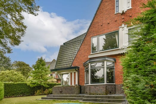A stylish modern home featuring large windows, a well-maintained garden, and a beautiful sky backdrop. The architecture blends contemporary design with natural elements.