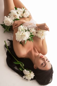 From above side view of sensual young female with bouquet of white flowers looking at camera on white background