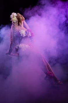 Side view of confident sensual young female model with long curly hair covering naked breast with fresh flowers in smoke