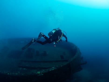 unrecognizable scuba diver diving into the blue ocean near of a wreck, concept of underwater adventure and active leisure lifestyle, copyspace for text