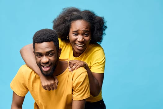 A joyful African couple wearing matching yellow shirts, smiling and playfully interacting against a bright blue background Ideal for themes of love, happiness, and relationships