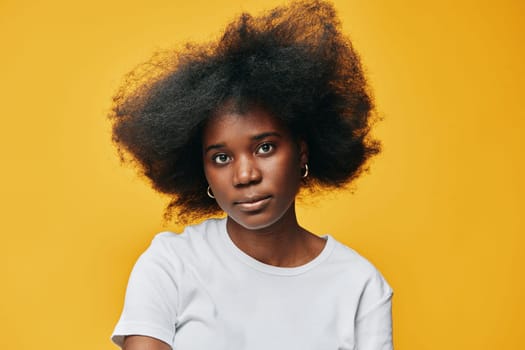 Confident Black female model with natural hair in a white t shirt, set against a bright yellow background, embodying beauty and empowerment