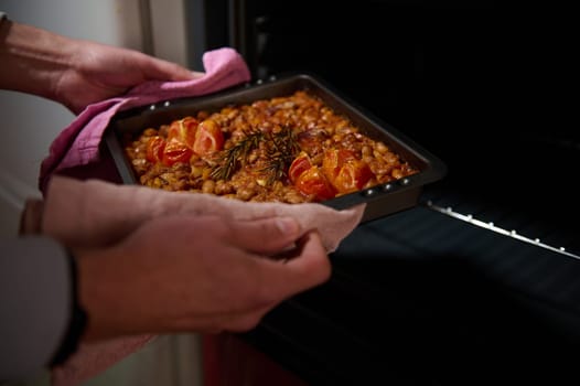 Home-cooked dish featuring baked beans with cherry tomatoes and rosemary, freshly taken out of the oven, capturing the warmth of homemade meals.