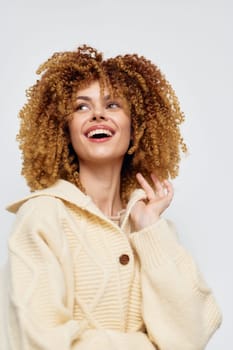 A cheerful woman with curly hair smiles brightly wearing a cozy beige sweater against a light background Her carefree expression exudes joy and natural beauty, perfect for fashion and lifestyle insp