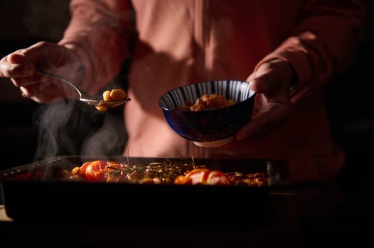 Close-up of a person plating a warm, steamy dish into a blue-striped bowl, focusing on the comforting and home-cooked nature of the meal. Backlit with cozy tones.
