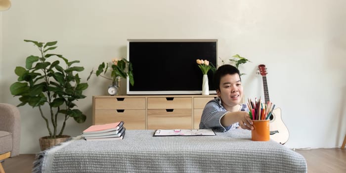 The teenage girl with Down syndrome engages in her art project, reaching for colorful supplies to enhance her creativity in a supportive environment.