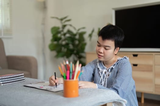 In a serene home environment, a teenage girl with Down syndrome expresses herself through drawing, highlighting her artistic exploration and creativity.