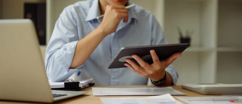 Businessperson analyzing data on digital tablet while seated at a desk.