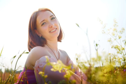 A joyful woman sits in a vibrant field, surrounded by wildflowers on a bright sunny day, radiating happiness and tranquility.