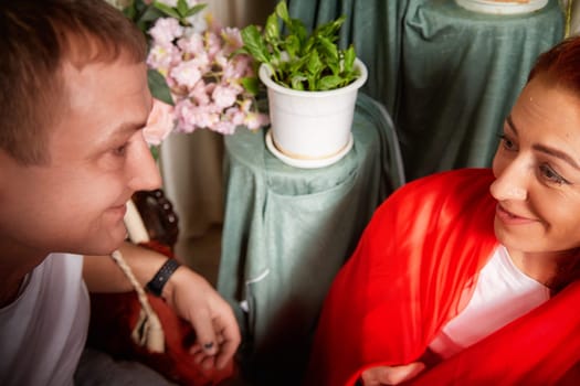 A middle-aged couple dressed in vibrant oriental attire share joyful moments while engaging in playful role-playing at home.